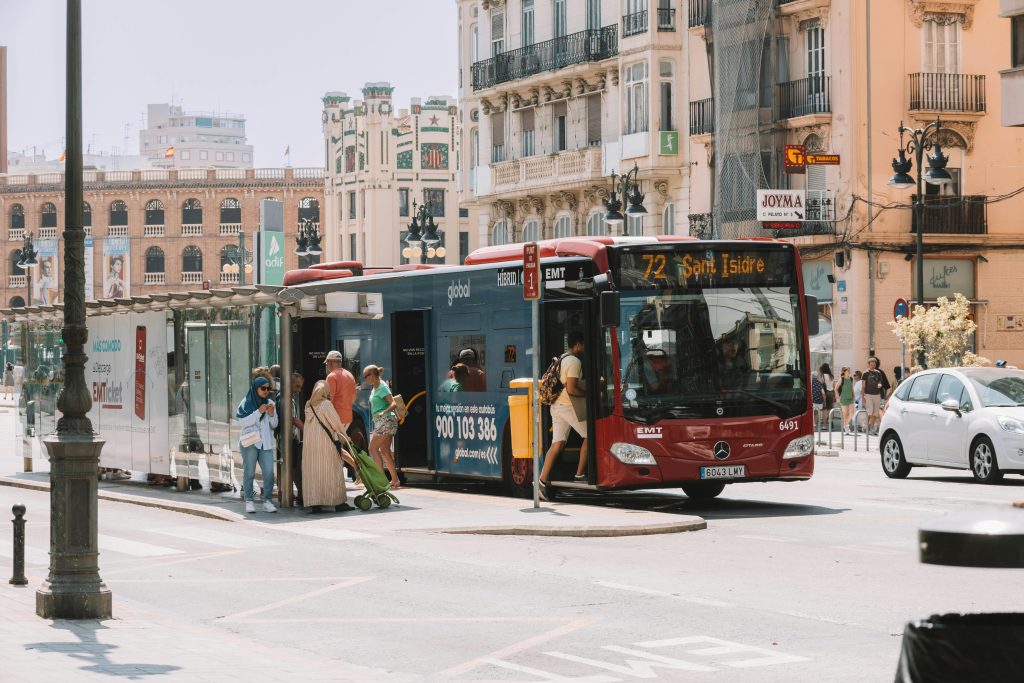 City bus at a stop in Valencia, Spain, with people boarding in a sunny urban setting.