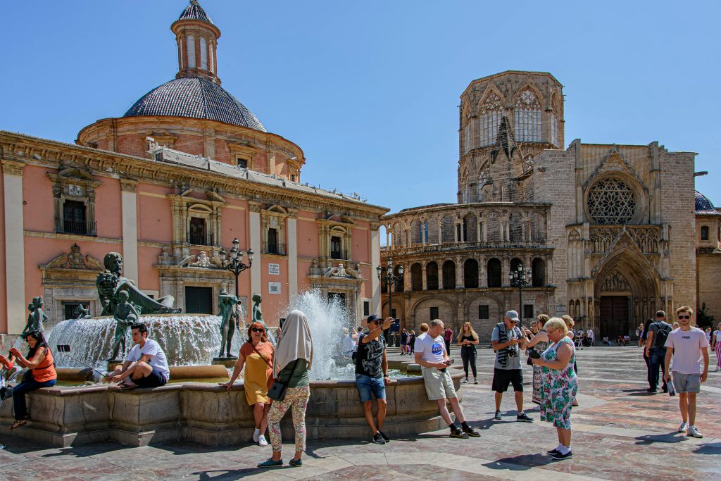 Tourists enjoy a sunny day at Plaza de la Virgen in Valencia with the cathedral in the background.