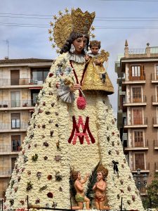 Ornate floral statue of the Virgin Mary in Valencia's city square during a festival.